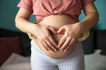 Wall Mural - Pregnant woman with her daughter holding her belly and making a heart shape.