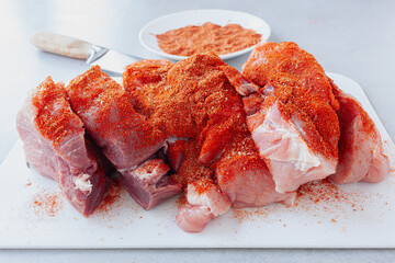 Wall Mural - Raw pork tenderloin covered in dry rub spices and cut in smaller pieces ready for roasting, plate with spices in background