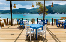 Outdoor  Greek  Restaurant With Blue Chairs And Tables And Sea View