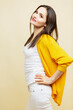 © Анна Демидова - Smiling young woman. Beautiful brunette in white pants and a yellow sweater. Light yellow background. Vertical.