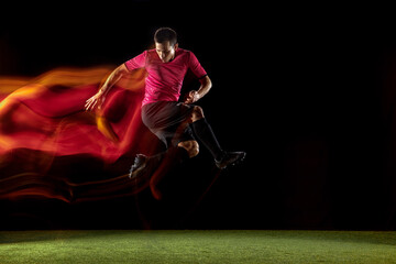 Powerful, flying above the field. Young football, soccer player in action, motion on black background in mixed neon light. Concept of sport, movement, energy and dynamic, healthy lifestyle.