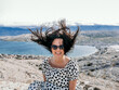 © Marko Klarić/Wirestock - Smiling Caucasian woman in a polka dots flowy dress and sunglasses with hair blown up by the wind