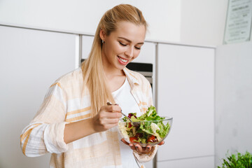 Joyful blonde woman smiling while preparing fresh salad