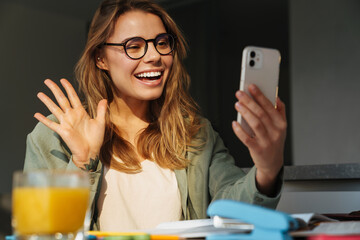 Wall Mural - Happy nice student woman waving hand while taking selfie on cellphone