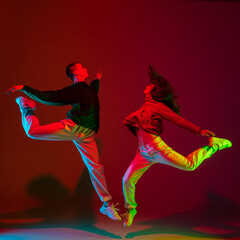 Wall Mural - Flying. Stylish sportive couple dancing hip-hop in stylish clothes on colorful background at dance hall in neon light. Youth culture, movement, style and fashion, action. Fashionable bright portrait.