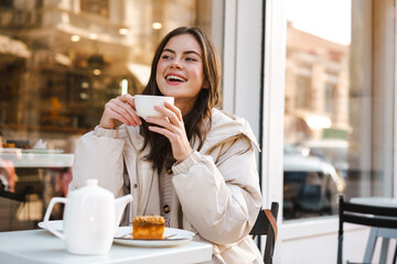 Wall Mural - Cheerful young woman having tea with cake