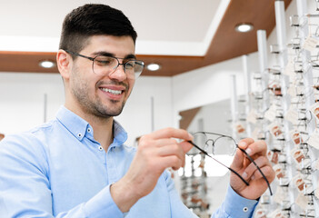 Fototapete - Portrait of happy young male customer choosing eyeglasses