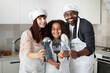 © sofiko14 - Family in hats and aprons, handsome African father, pretty Caucasian mother and cute teen mixed race girl, holding cooking devices and showing it to camera