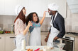 © sofiko14 - Baking is fine and funny. Happy curly mixed race teen girl smutching her father's face with flour, while having fun with her parents in the kitchen, baking together