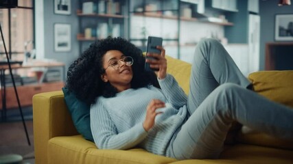 Aufkleber - Happy Young Latina with Afro Hair Jumping Over on a Sofa Couch at Home while Using a Smartphone. Beautiful Diverse Multiethnic Hispanic Female Browsing the Web and Chatting with Friends.