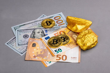 Economic concept: Crypto currency, money and gold on global stock markets. Three shiny bitcoin and two gold pieces lying on some EURO and US dollar banknotes. Grey background with copy space