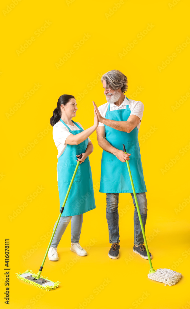 Mature couple with floor mops giving each other high-five on color background