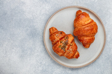 Wall Mural - Freshly baked homemade croissants for breakfast. Traditional and whole-grain croissant with pumpkin seeds in a gray plate on a concrete or stone background. Selective focus, copy space