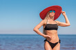 © mavrik - sporty woman in black swimsuit and red hat stands on the beach against the background of blue sky and sea. sport and recreation concept