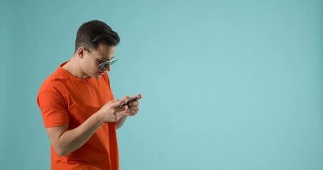 Wall Mural - young man with mobile phone playing game on color background