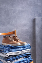 Denim Jeans And Old Leather Boots Shoes At Wooden Chair Near Grey Wall Background