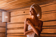 Happy woman relaxing in wooden sauna on blurred background