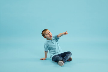 Wall Mural - Pointing. Childhood and dream about big and famous future. Pretty little boy isolated on blue studio background. Dreams, imagination, education, facial expression, emotions concept.