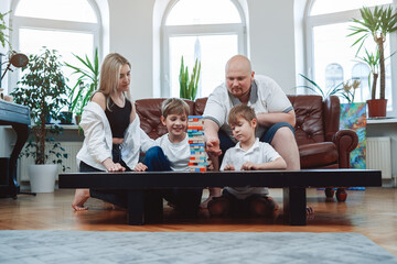 Couple of caucasian man and woman constructing a tower from bricks with their two little boys in modern living room.