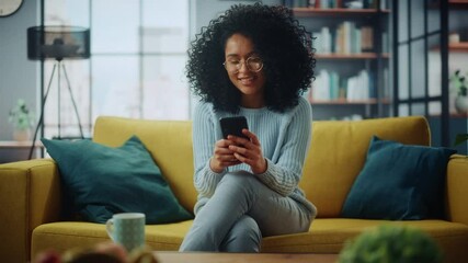 Aufkleber - Portrait of a Beautiful Authentic Latina Female in a Stylish Cozy Living Room Using Smartphone at Home. She's Browsing the Internet and Checking Videos on Social Networks and Having Fun.
