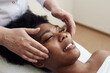 © etonastenka - Smiling black woman enjoying a toning facial massage. Serene woman relaxing outdoor in a beauty center