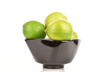 Group of green, organic lime in a black ceramic plate, on a white background.