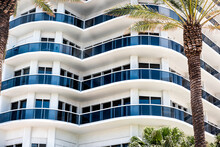 Abstract View On Residential Apartment Complex Building With Many Windows, Balconies Painted In White Blue On Sunny Day With Palm Trees