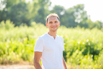 Bokeh green soft meadow background in nature park with portrait of smiling young happy man in summer in white shirt