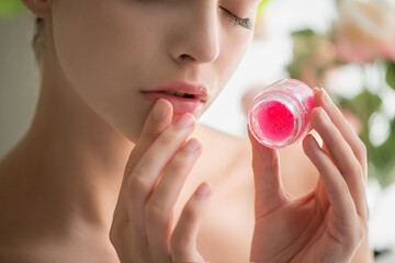 Beautiful young woman with clean perfect skin uses lips sugar scrub.