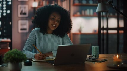 Poster - Beautiful Authentic Latina Female Sitting at a Desk in a Cozy Dark Living Room in the Evening and Using Laptop Computer at Home