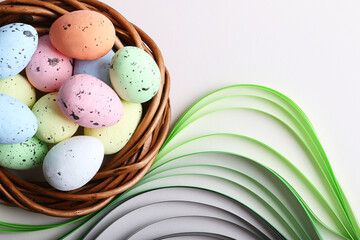 Colorful easter eggs in the rattan nest on the pastel grey background.Green paper like grass under it.Creative layout with copy space.