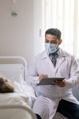 Poster - Male doctor in whitecoat and protective mask making notes in medical document