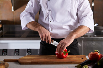 cropped man cuts ripe red peppers in restaurant kitchen. Cutting Bell Pepper indoors. Cooking fresh, ripe, bell pepper salad for guests. Summer fresh vegetable salad.