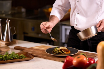 Cook dressing salad with sauce, pouring sauce into plate, finishing cooking of meal in restaurant kitchen, cropped man in apron at work