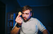 © bodnarphoto - Bearded hungry man sits at night in a room with a blue light on his desk and looks at the chips in his hand with a serious face. Snack on chips at night.