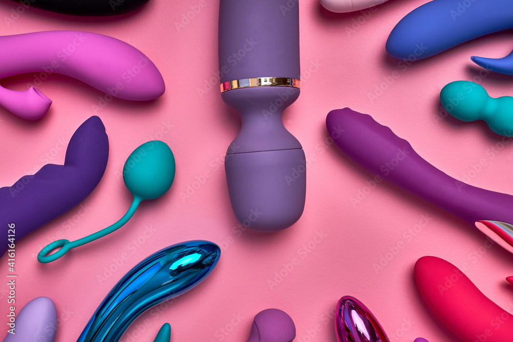purple big phallus among small sex toys isolated on pink background, a lot  of bright vobrators lie on pink paper, toys for relaxation and pleasure,  romantic time. sex shop concept Stock-foto |
