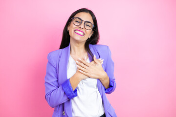 Wall Mural - Young business woman wearing purple jacket over pink background smiling with her hands on her chest and grateful gesture on her face.