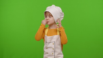 Wall Mural - Charming child girl dressed in apron and hat like chef cook showing approval ok sign, tasty gesture on chroma key background. Concept of nutrition, family cooking school, children education, game