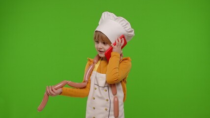 Wall Mural - Child girl kid dressed as cook chef receiving online order, talking on mobile phone, making conversation call with client. Chroma key background. Nutrition, cooking food, restaurant.