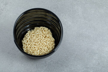 A black bowl with uncooked noodles on a gray background