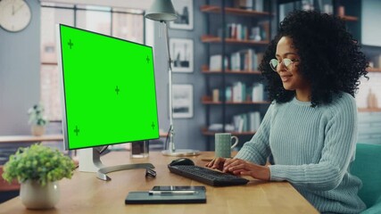 Poster - Latina Female Specialist Working on Desktop Computer with Green Screen Mock Up Display at Home Living Room while Sitting at a Table. Freelancer Female Chatting Over the Internet on Social Networks.