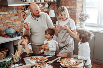 Warm portrait of a happy and young family they taste a domestic pizza. Loving couple and their children in the kitchen.