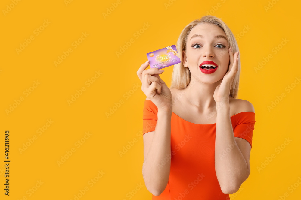 Surprised young woman with gift card on color background
