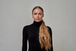 Portrait of beautiful caucasian female model with long hair wearing black turtleneck looking at camera, standing isolated over gray background