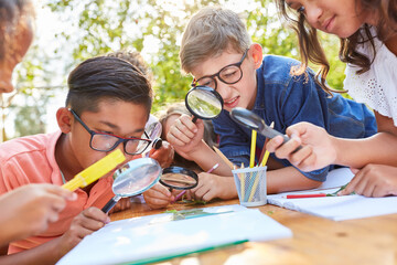 group of children with magnifying glass curiously look at a leaf