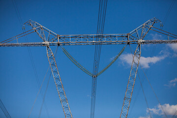 Electric pylon (pole) and glass insulators on blue sky with light clouds background. Close-up photo.