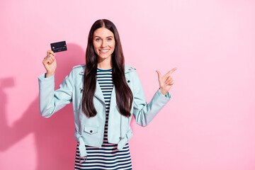 Sticker - Photo of young happy woman wear striped dress blue leather jacket point empty space hold credit card isolated on pink color background