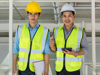 Two engineers in yellow reflective vest and wearing safety hardhat working together in consruction site