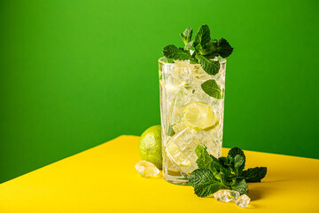 Wall Mural - Mojito cocktail with lime and mint in highball glass green yellow background. Summer cold beverages concept with copy space