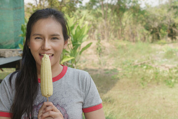 A lady is about to eat boiled sweet corn on a stick.